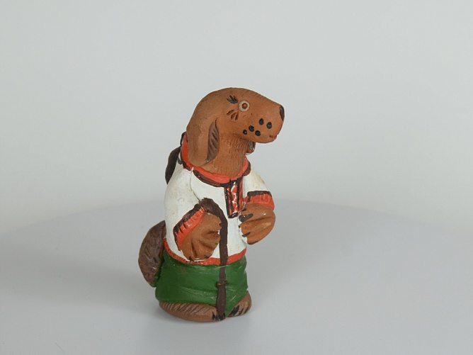 Собака-игрушка. Собака в рубахе и штанах, из красной глины. В правой передней лапе держит посох, за спиной - рюкзак. М.: глина; Т.: лепка, обжиг, роспись. Высота - 11,5 см.